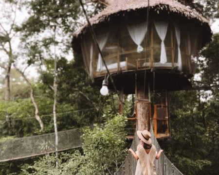 A woman standing on a treehouse in the jungle.